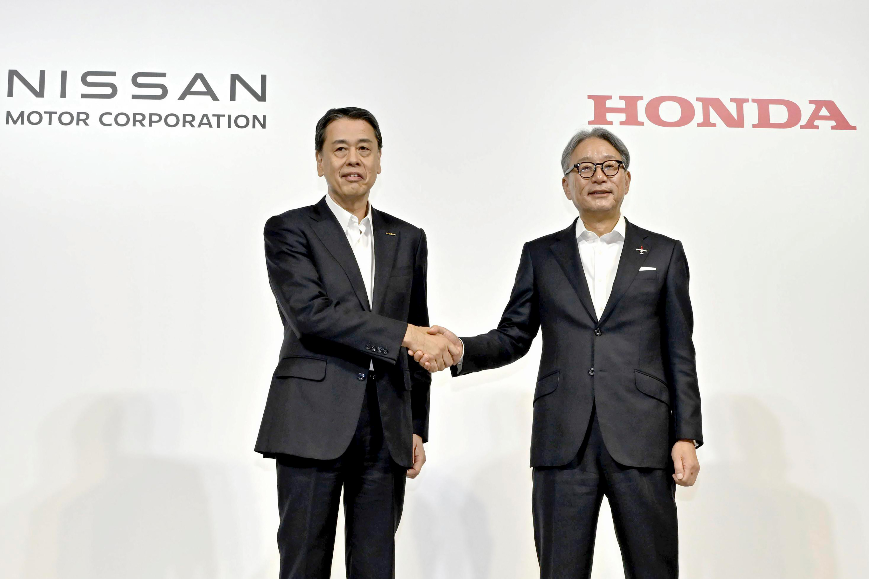 Nissan Chief Executive Makoto Uchida, left, and Honda Chief Executive Toshihiro Mibe shake hands during a joint news conference in Tokyo, Thursday.