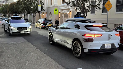Two Waymo driverless taxis stop before passing one another on a San Francisco street on Feb. 15, 2023.