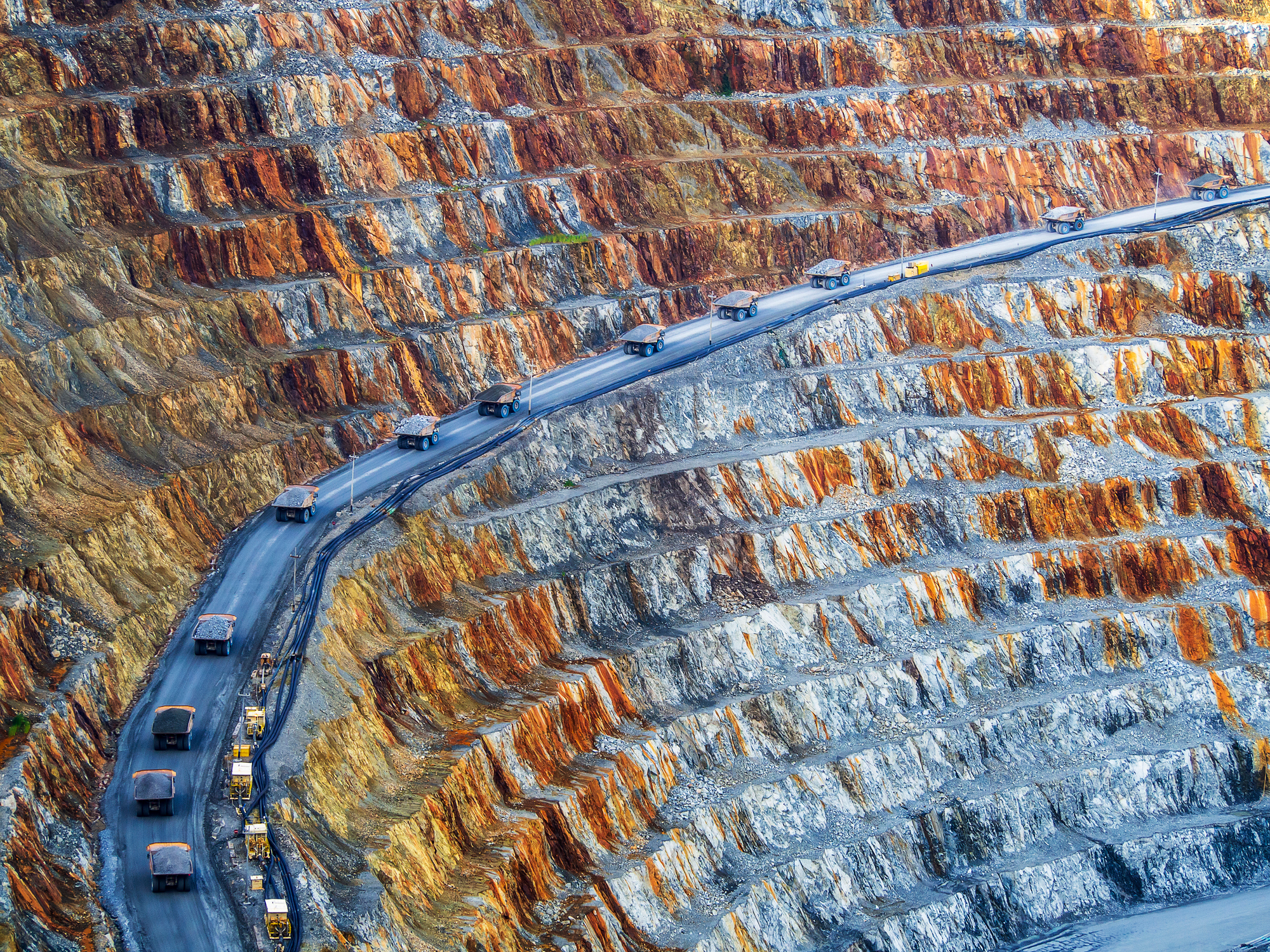 A dump truck convoy travels up through a copper mine.
