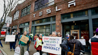 People protesting Elon Musk's actions in the Trump administration hold signs outside a Tesla showroom in Seattle on Thursday, Feb. 13, 2025.