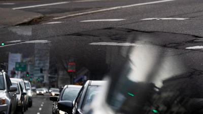 In this image taken through the reflection of a car window, a person walks along W Burnside Street near a repaired patch in the road on Thursday, Feb. 6, 2025, in Portland, Ore.