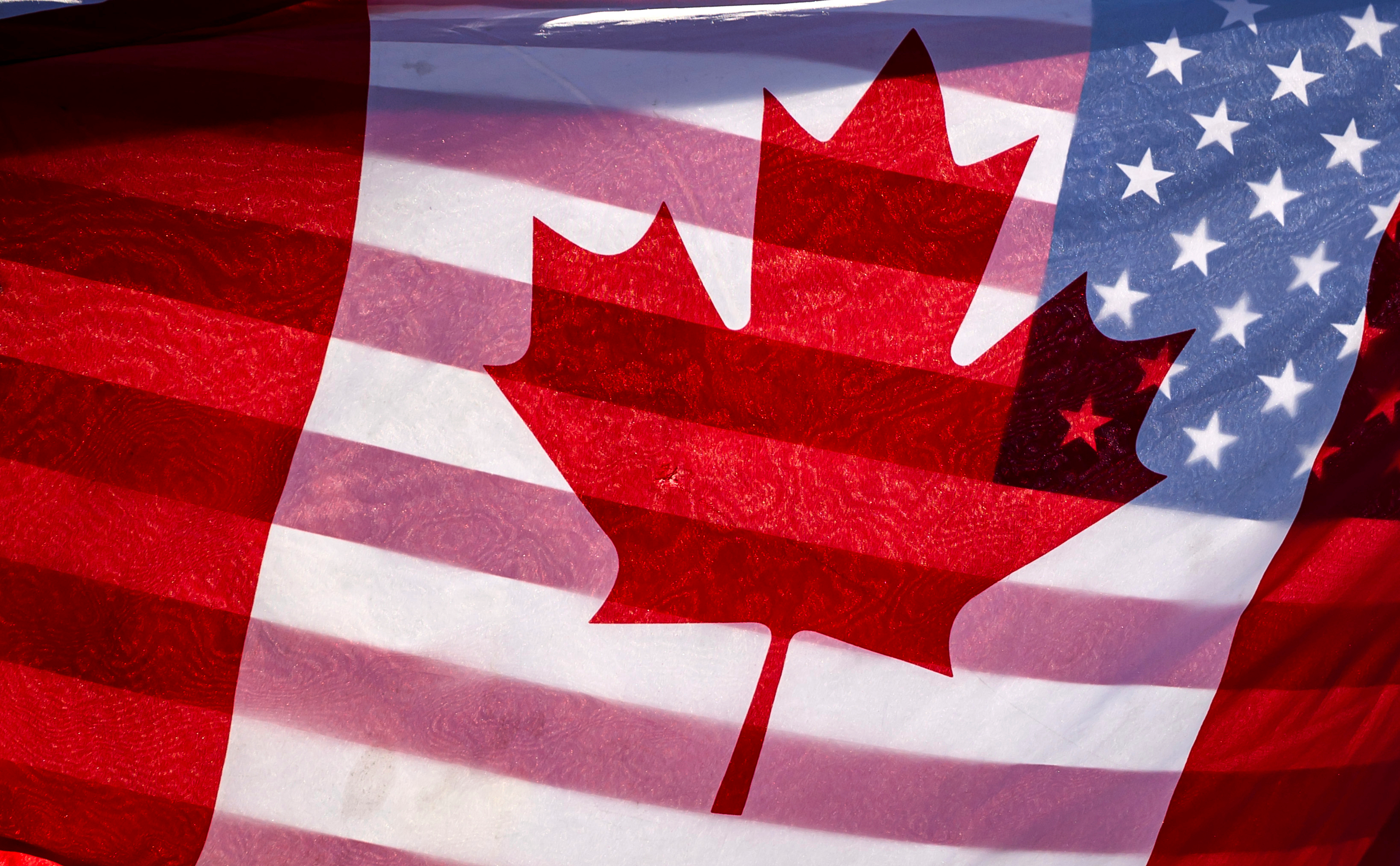 Sunlight shines through the flags of Canada and the United States, held together by a protester outside on Parliament Hill in Ottawa, Feb. 1, 2025.