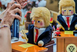 A woman uses hairspray to fixe the hair on a nutcracker titled 'Resolute Desk of the President,' featuring a seated figure signing a 'presidential proclamation,' at the Steinbach-Volkskunst nutcracker factory in Marienberg, Germany, Tuesday, April 15, 2025.