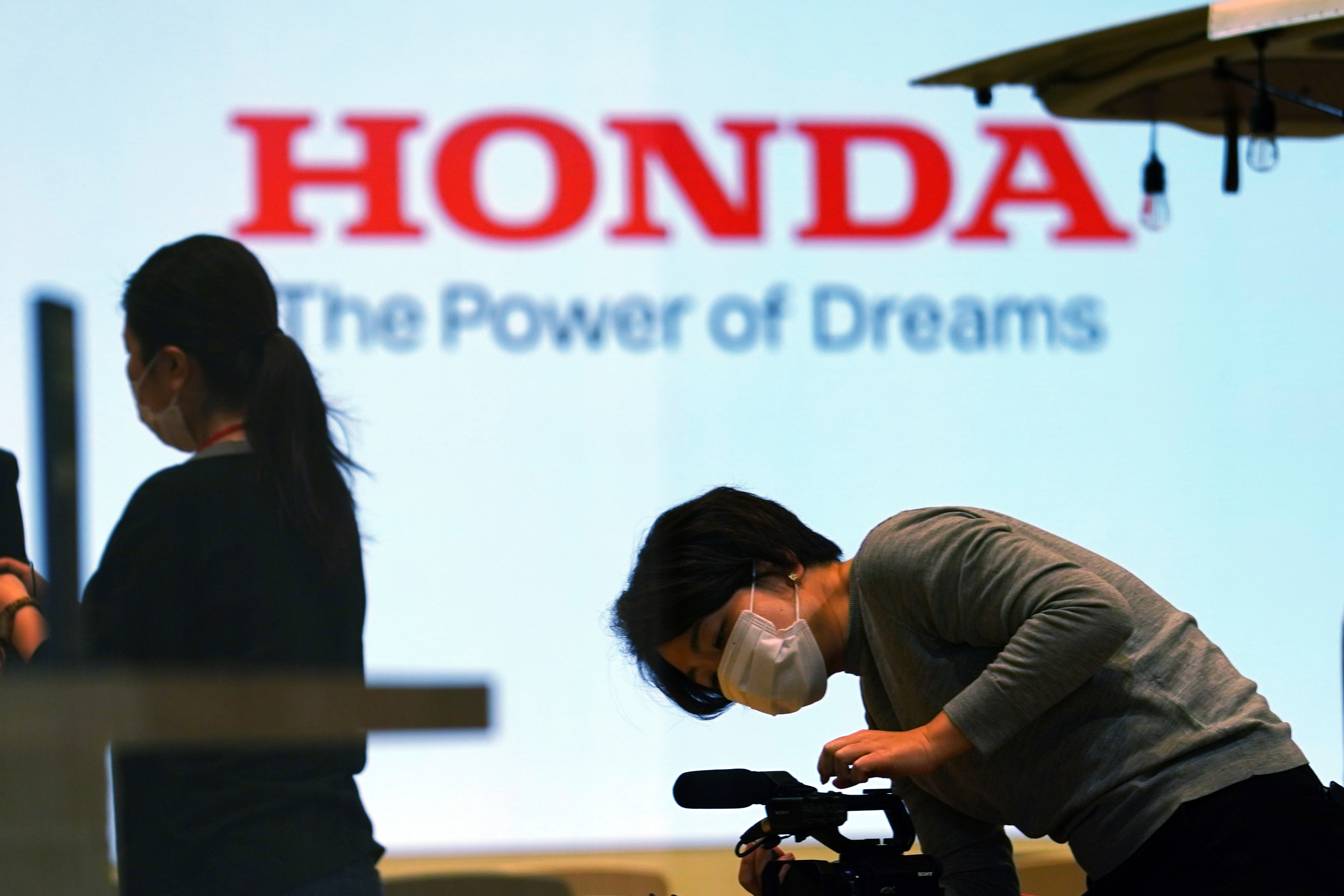 A woman wearing a protective mask to help curb the spread of the coronavirus works near the logo of Honda Motor Company at a showroom on May 13, 2021, in Tokyo.
