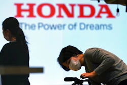 A woman wearing a protective mask to help curb the spread of the coronavirus works near the logo of Honda Motor Company at a showroom on May 13, 2021, in Tokyo.