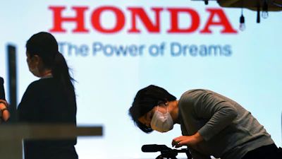 A woman wearing a protective mask to help curb the spread of the coronavirus works near the logo of Honda Motor Company at a showroom on May 13, 2021, in Tokyo.