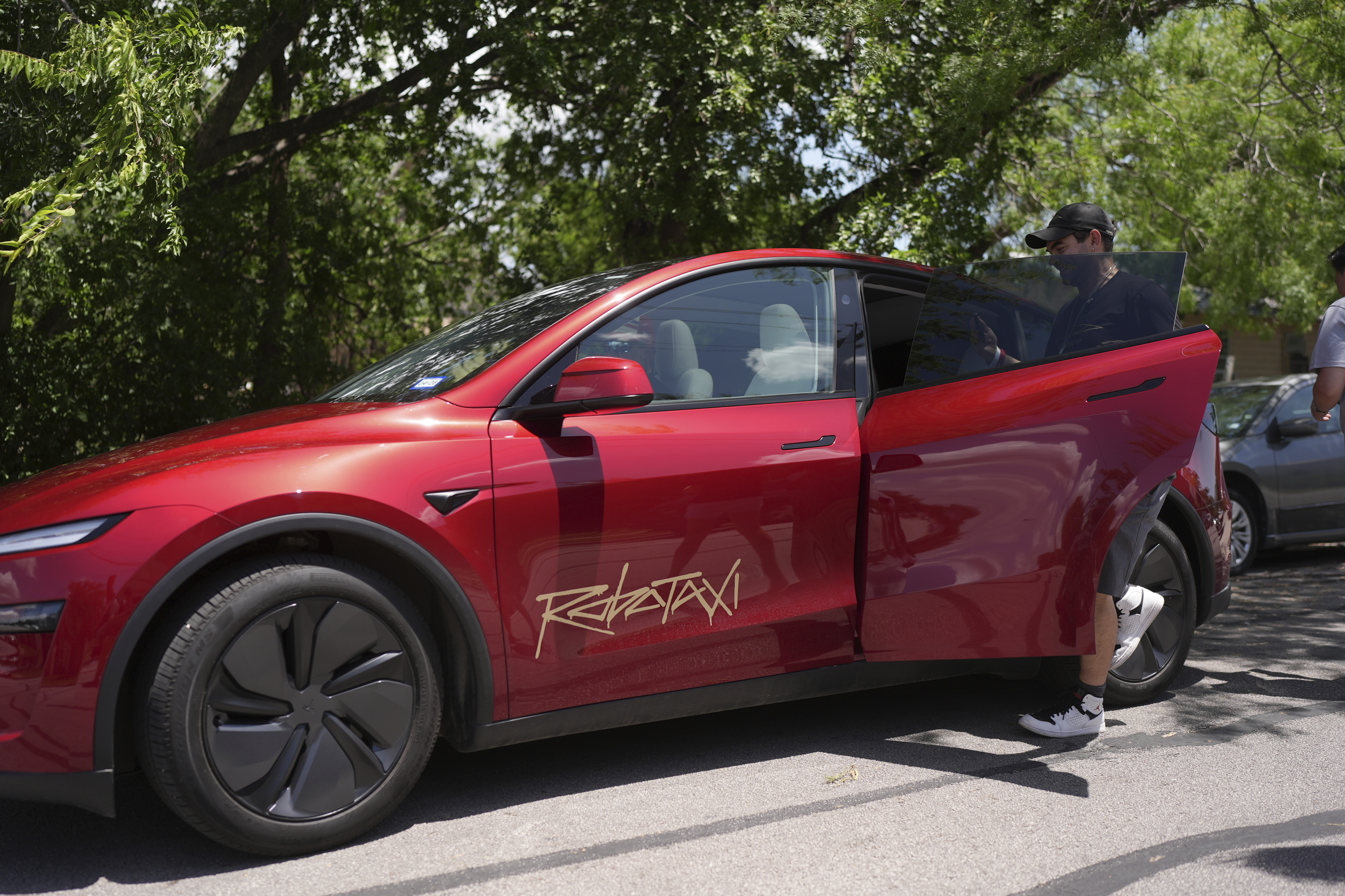 Red Tesla electric vehicle parked under trees with open door