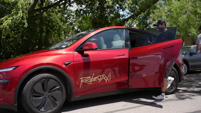 Red Tesla electric vehicle parked under trees with open door