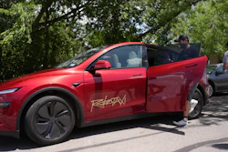 Red Tesla electric vehicle parked under trees with open door
