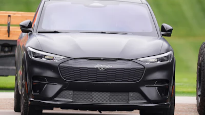 Black Ford Mustang Mach-E electric SUV parked on road with green background