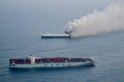 Two cargo ships at sea, one emitting thick smoke against a gray maritime horizon