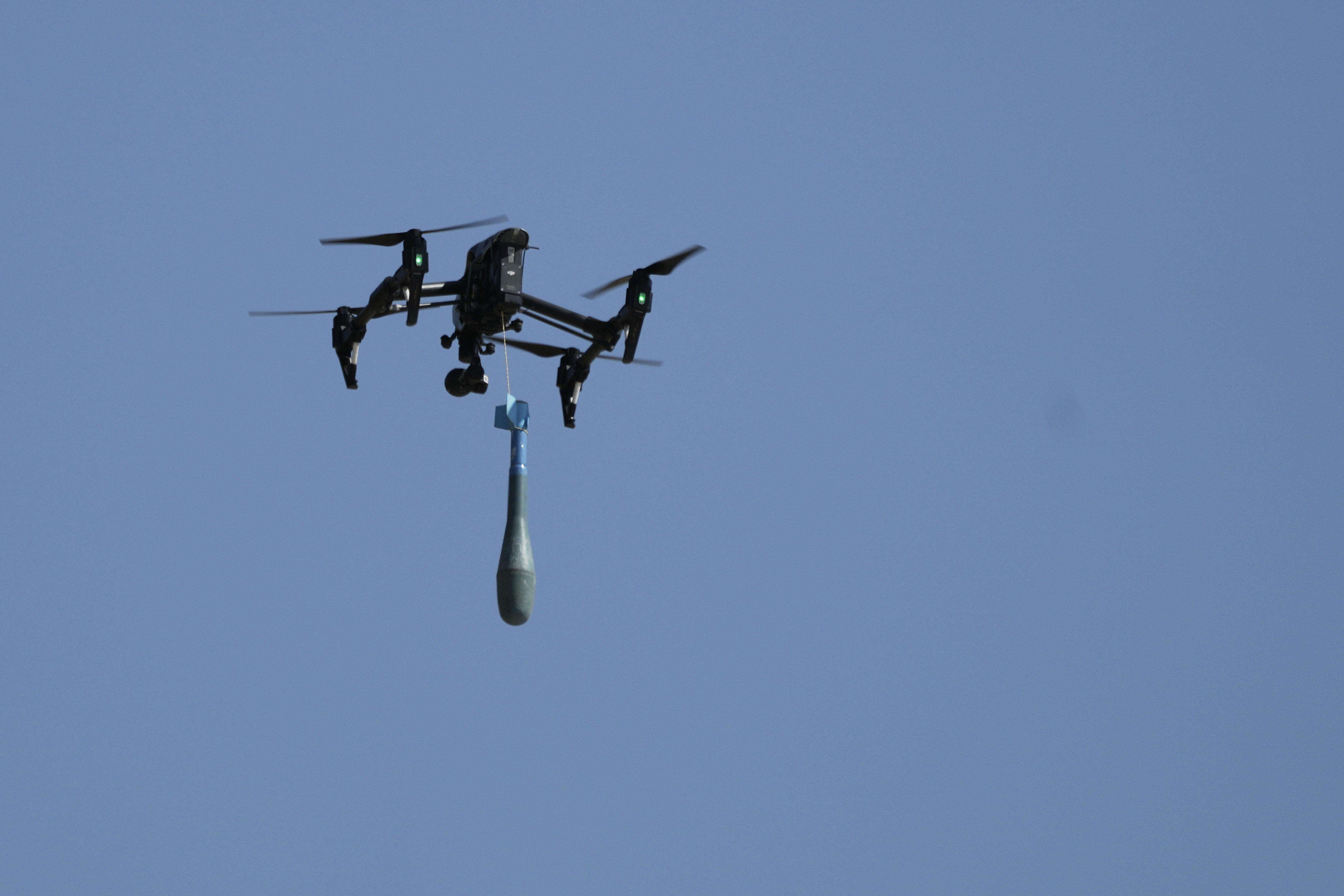 Quadcopter drone flying with suspended payload against blue sky