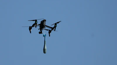 Quadcopter drone flying with suspended payload against blue sky