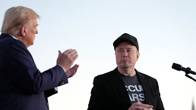 Political figures at a press conference, one applauding while the other stands stoically