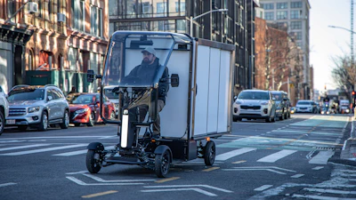 Enclosed electric delivery vehicle on city street with urban buildings