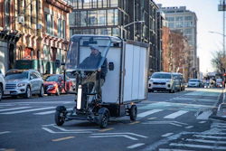 Enclosed electric delivery vehicle on city street with urban buildings