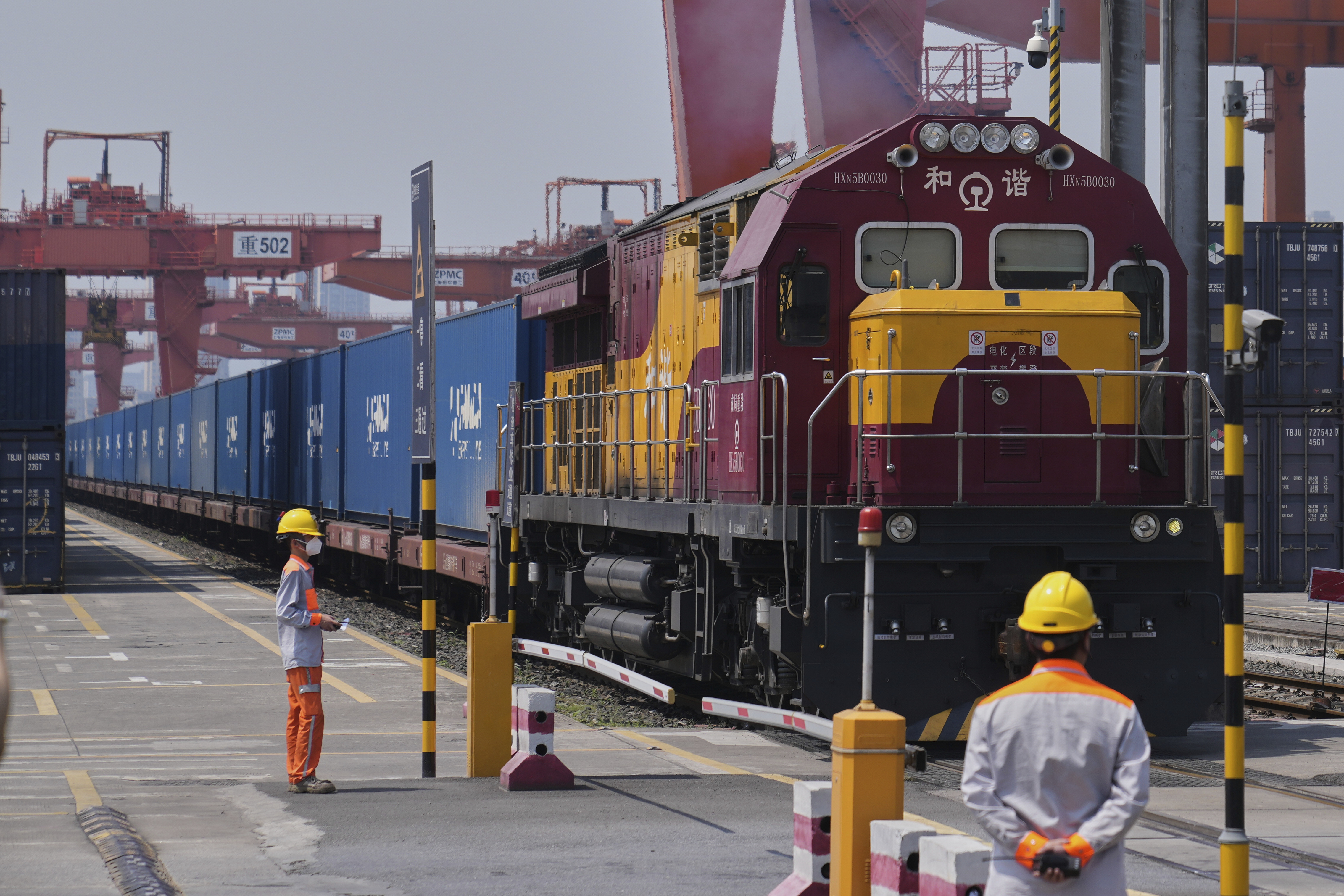 Maroon and yellow freight locomotive with blue shipping containers at industrial port