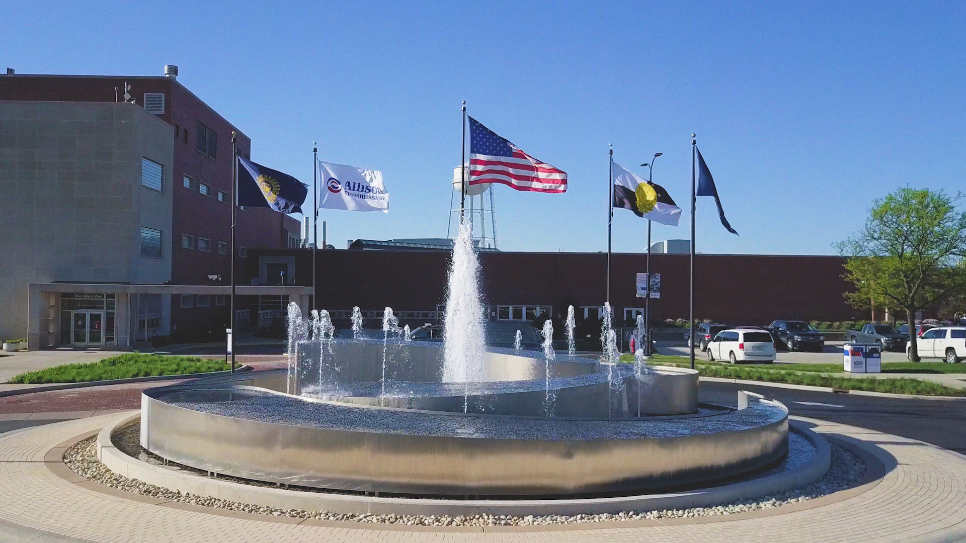 Water fountain with multiple flags in front of brick government building on sunny day
