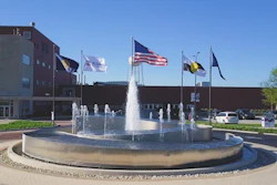 Water fountain with multiple flags in front of brick government building on sunny day