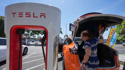 Tesla electric vehicle charging at a white and red Supercharger station