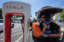 Tesla electric vehicle charging at a white and red Supercharger station
