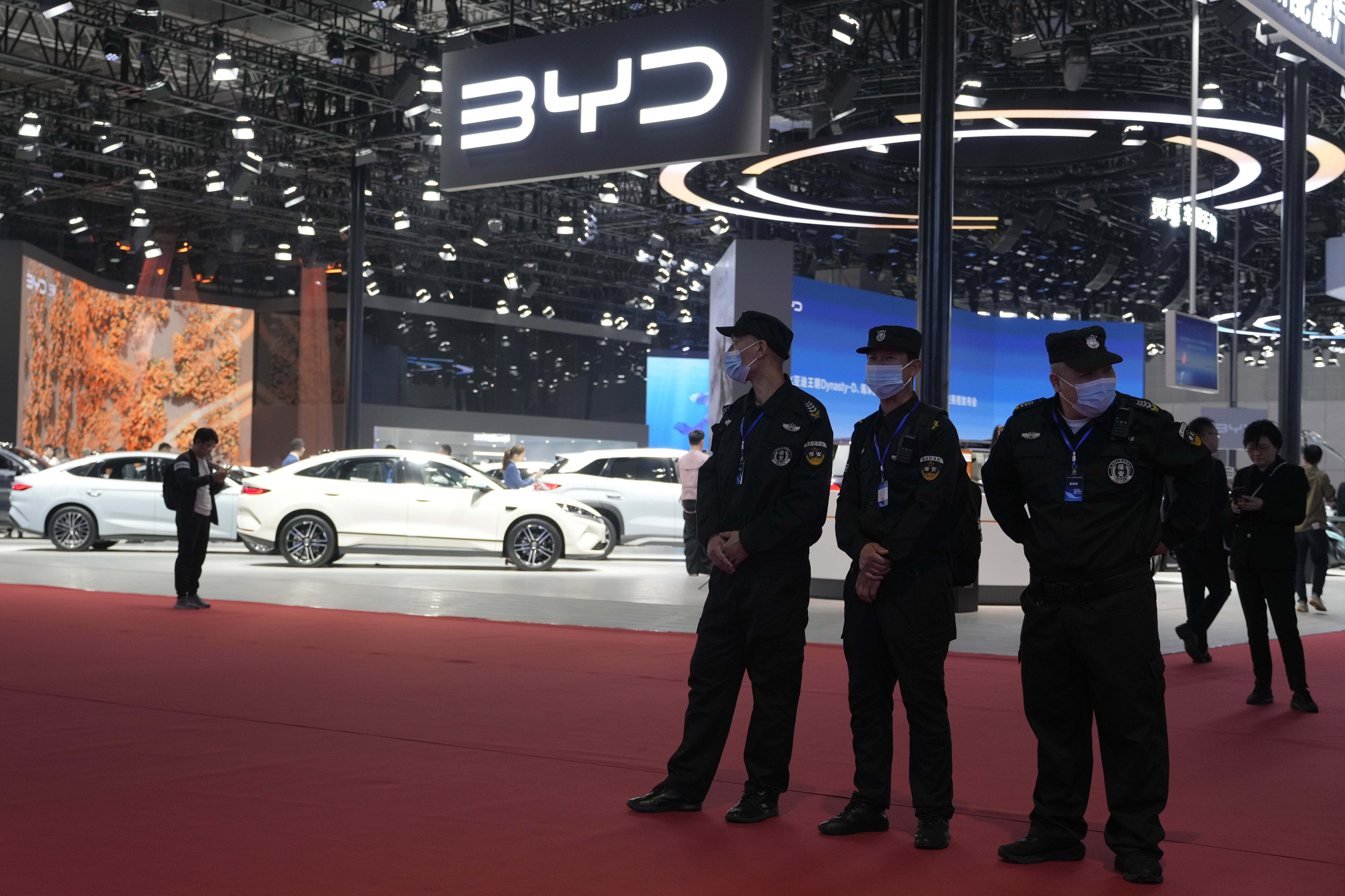 BYD automotive booth at car show with white vehicles and security personnel