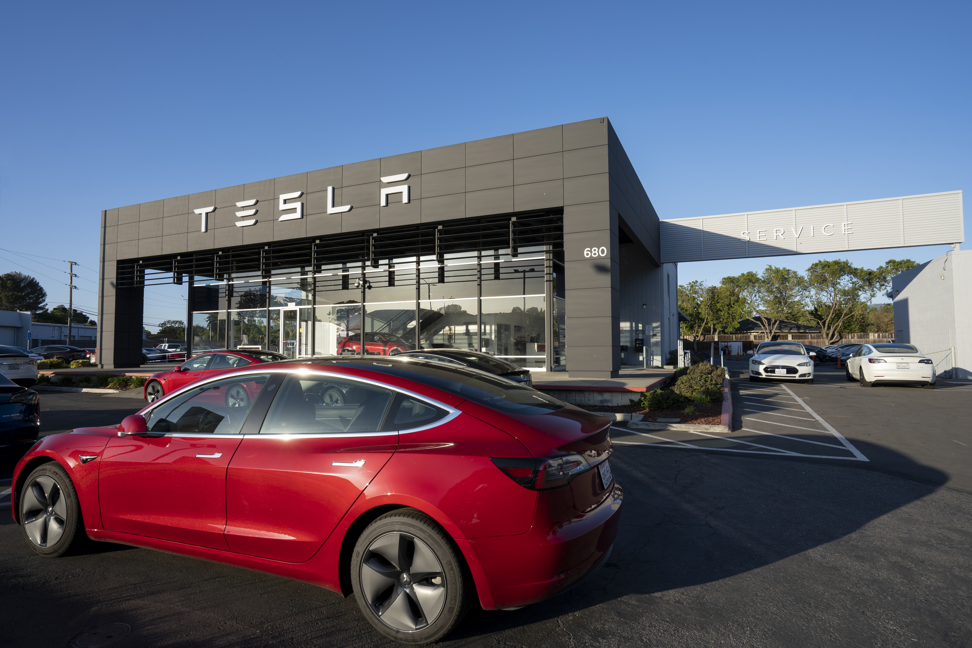 Red Tesla electric car parked in front of modern Tesla dealership with glass facade