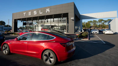 Red Tesla electric car parked in front of modern Tesla dealership with glass facade