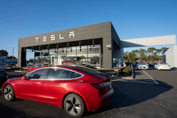 Red Tesla electric car parked in front of modern Tesla dealership with glass facade