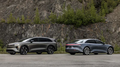 Two luxury electric vehicles parked beside rocky cliff with green vegetation