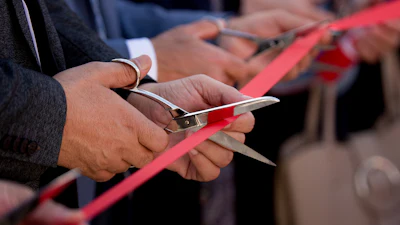 Hands cutting red ribbon at official opening ceremony