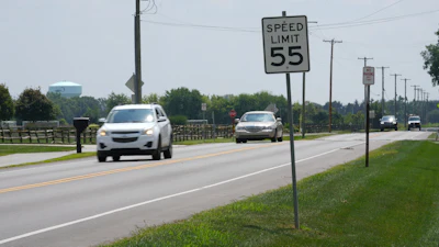 Highway with 55 mph speed limit sign, white and gray vehicles driving on road