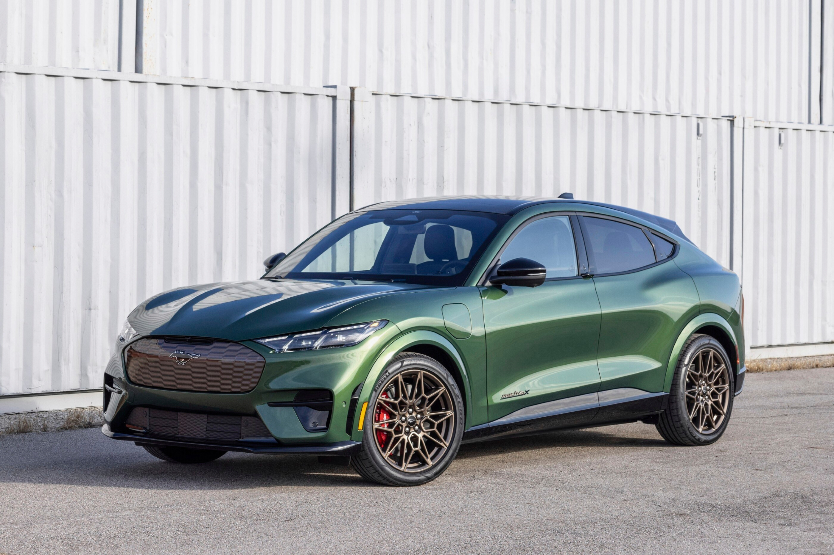 Dark green Ford Mustang Mach-E electric SUV parked against white container background