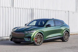 Dark green Ford Mustang Mach-E electric SUV parked against white container background