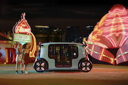 Autonomous white vehicle parked near neon-lit Flame restaurant and glowing architectural structure at night