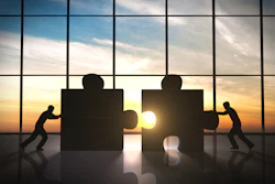 Silhouettes pushing puzzle pieces together at sunset, symbolizing teamwork and collaboration