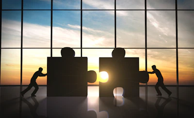 Silhouettes pushing puzzle pieces together at sunset, symbolizing teamwork and collaboration