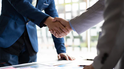 Business professionals shaking hands over financial documents and charts during a meeting