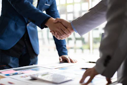 Business professionals shaking hands over financial documents and charts during a meeting