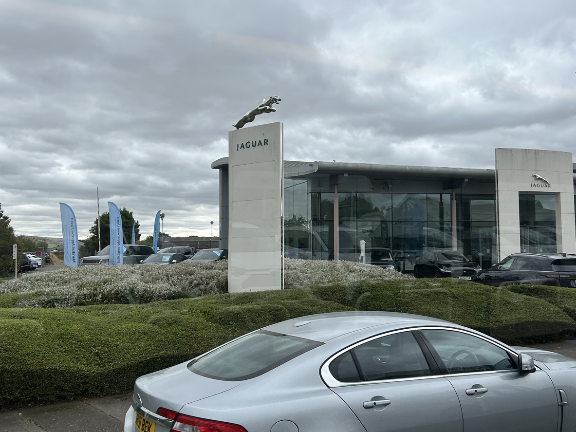 Jaguar car dealership with silver car, glass showroom, and cloudy sky