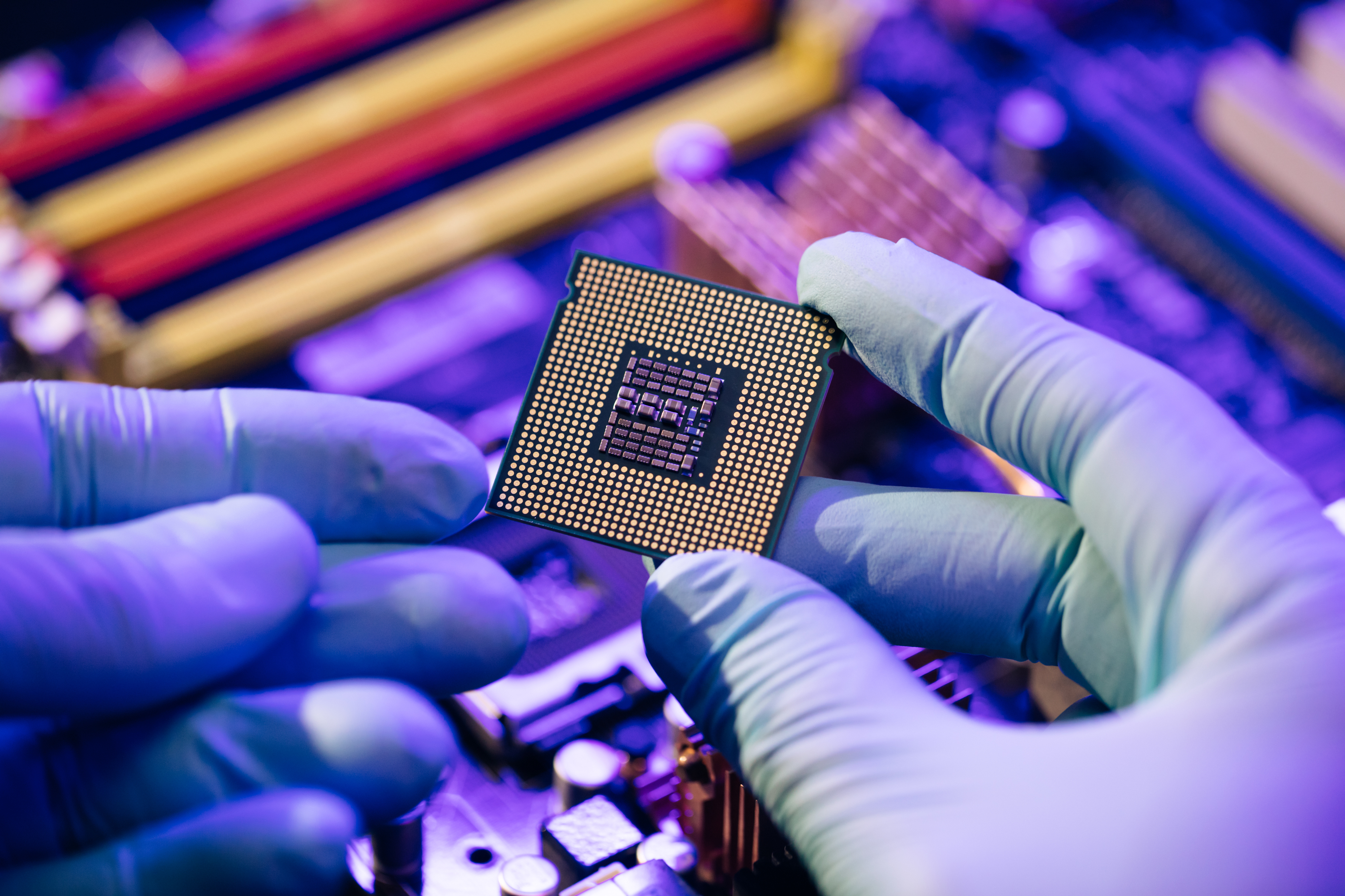 Gloved hands carefully holding a computer microprocessor chip in a purple-tinted tech environment