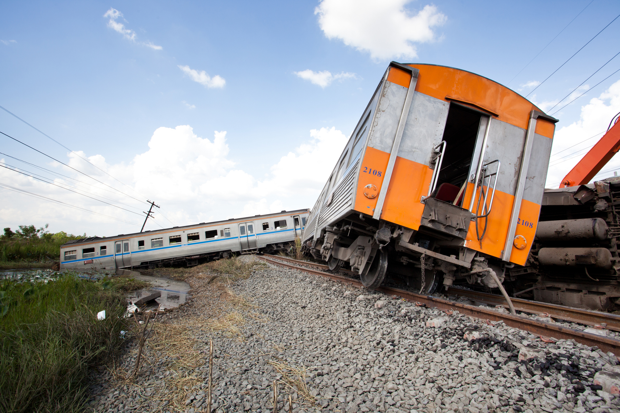 Train derailment with orange and silver train cars off damaged railroad tracks