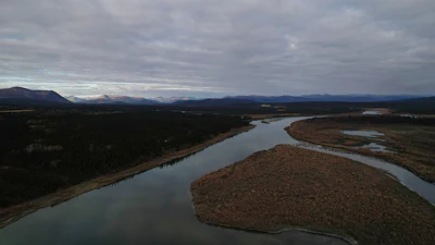Winding river through forested valley with distant mountain ranges under cloudy sky