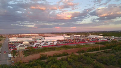 Sunset over industrial complex with white arched buildings and red perimeter fence