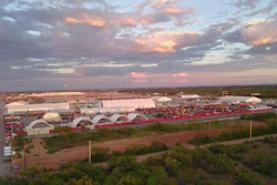 Sunset over industrial complex with white arched buildings and red perimeter fence