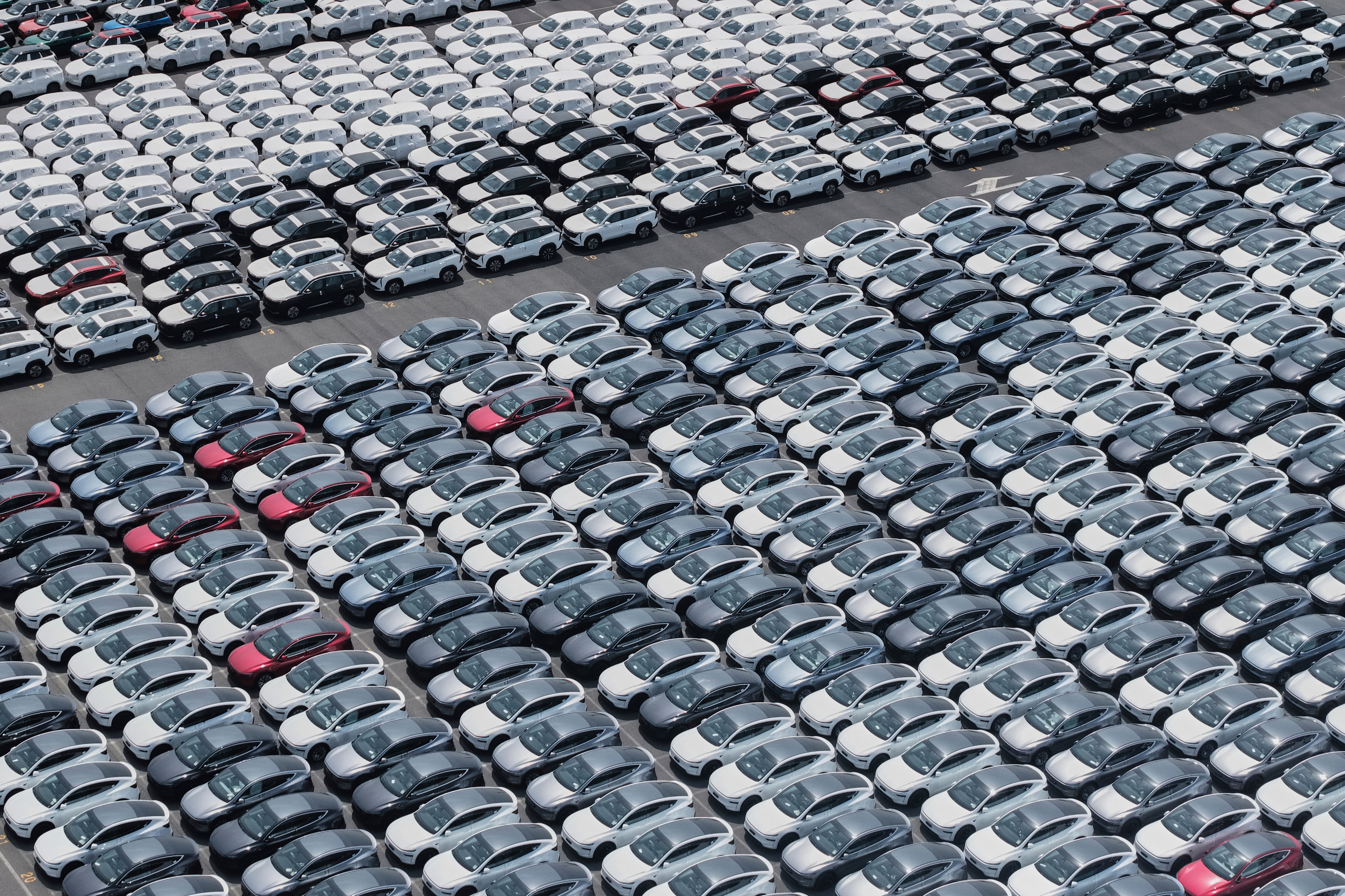 Aerial view of hundreds of white, gray, and red cars parked in tight rows