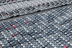 Aerial view of hundreds of white, gray, and red cars parked in tight rows