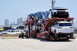 Car carrier trailer loaded with white SUVs at transportation facility