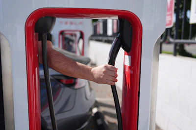 Red gas pump with hand holding black fuel nozzle at fueling station