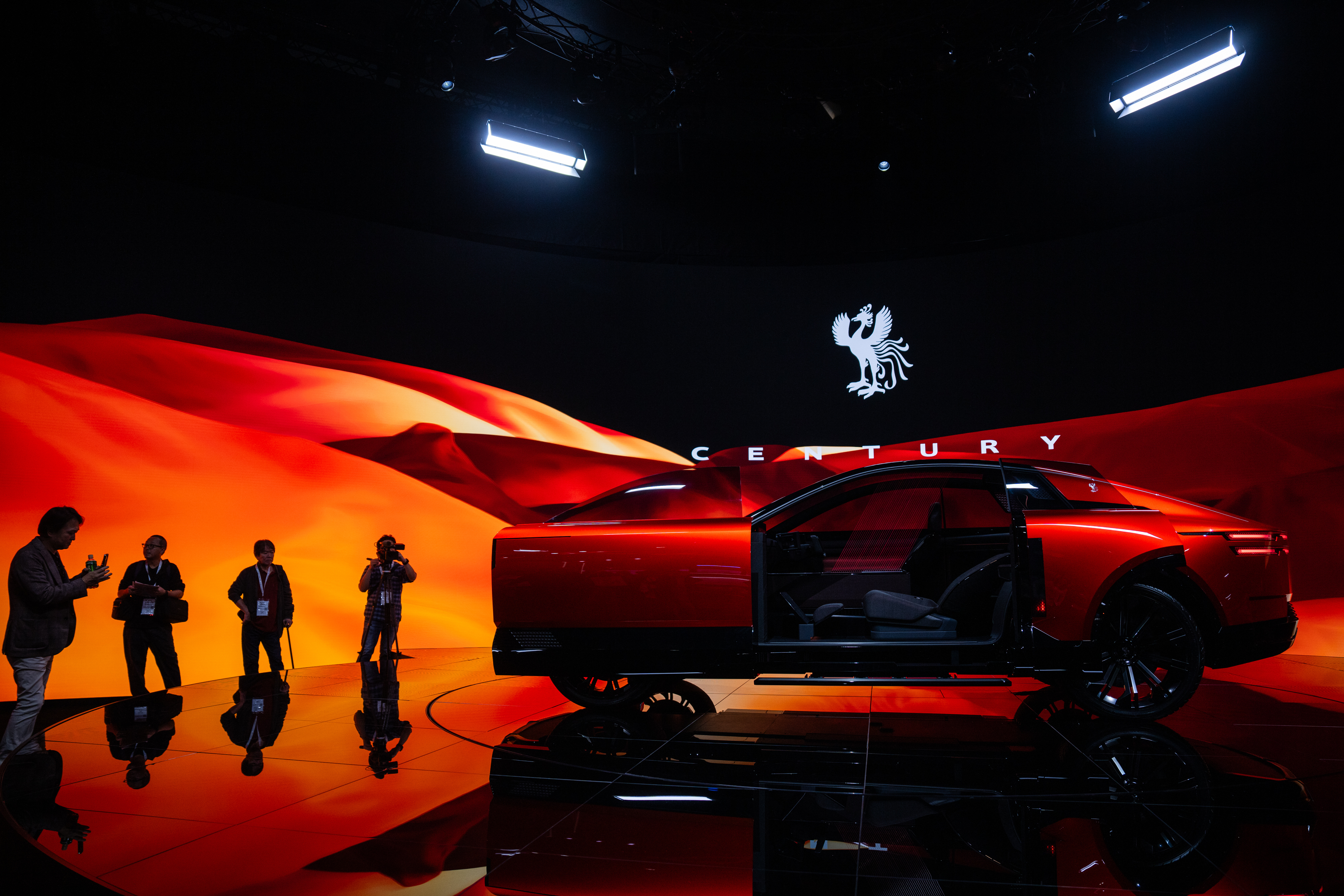 Red luxury concept car on stage with dramatic lighting and silhouetted figures
